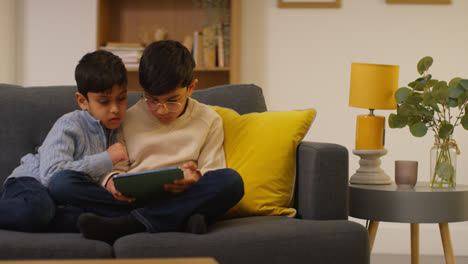 Two-Young-Boys-Sitting-On-Sofa-At-Home-Playing-Games-Or-Streaming-Onto-Digital-Tablet-9